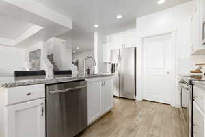 Kitchen with stainless steel appliances, white cabinets, light wood-style floors, light stone counters, and recessed lighting
