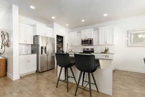 Kitchen with light stone counters, stainless steel appliances, white cabinets, an island with sink, and a kitchen breakfast bar
