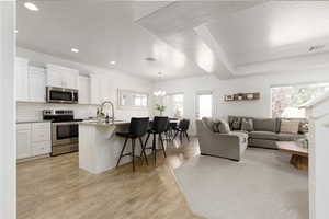 Living room with light wood finished floors, suspended lighting, and a textured ceiling
