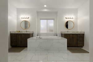 Full bathroom featuring a garden tub, two vanities, and light marble finish flooring