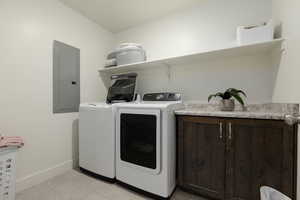 Laundry area with electric panel, separate washer and dryer, light tile patterned floors, and cabinet space