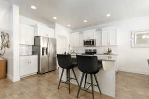 Kitchen with stainless steel appliances, light stone countertops, a kitchen island with sink, white cabinetry, and a kitchen breakfast bar