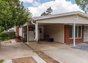 View of front of house featuring an attached carport, brick siding, driveway, and a patio