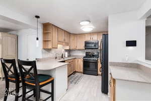 Kitchen with black appliances, a breakfast bar, a peninsula, hanging light fixtures, and light wood finish cabinets