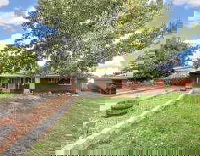 Ranch-style house featuring an attached carport, a front lawn, brick siding, and driveway