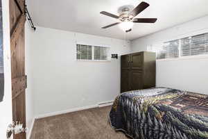 Bedroom with dark carpet, a barn door, a ceiling fan, and a baseboard radiator