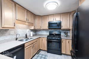 Kitchen featuring black appliances, light wood finish cabinets, light stone counters, and light wood-style floors