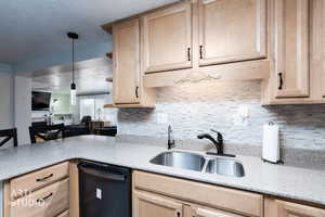 Kitchen featuring light wood finish cabinetry, black dishwasher, light stone counters, pendant lighting, and a textured ceiling
