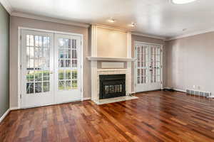 Unfurnished living room with french doors, crown molding, dark wood-type flooring, and a fireplace