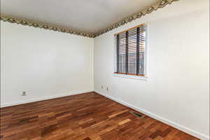 Spare room featuring dark wood-type flooring and baseboards