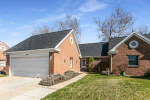 View of front facade with roof with shingles, a front lawn, brick siding, and driveway