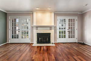 Unfurnished living room featuring french doors, ornamental molding, dark wood-style floors, and a premium fireplace