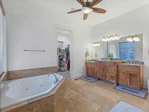 Primary bathroom with double vanity, a walk in closet, a whirlpool tub, and ceiling fan