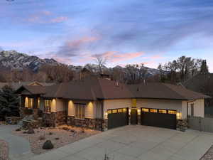 Prairie-style house featuring a garage, stone siding, concrete driveway, a gate, and a mountain view