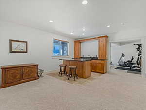 Wet bar featuring light colored carpet, wood finish cabinets, recessed lighting, and dark stone counters