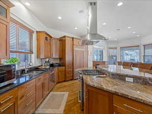 Kitchen with glass fronted cabinets, wood finish cabinetry, dark stone countertops, stainless steel appliances, and recessed lighting