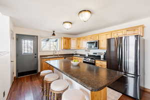 Kitchen featuring stainless steel appliances, a center island, a kitchen bar, and dark wood-style floors