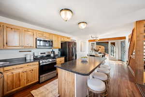 Kitchen featuring dark countertops, stainless steel appliances, a kitchen island, dark wood finished floors, and a breakfast bar area