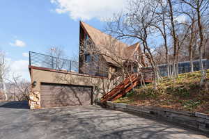 View of front of home featuring a garage, asphalt driveway, stone siding, and a deck