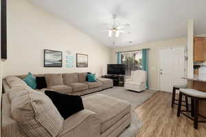 Living area featuring lofted ceiling, light wood-style floors, and a ceiling fan