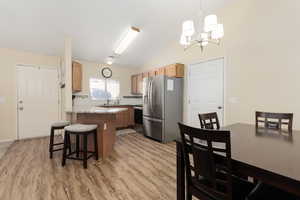 Kitchen with stainless steel appliances, vaulted ceiling, a kitchen bar, a chandelier, and light wood-style floors