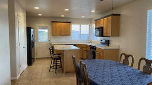 Kitchen with a kitchen breakfast bar, light countertops, a kitchen island, black appliances, and recessed lighting
