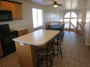 Kitchen featuring black appliances, a kitchen breakfast bar, a center island, light tile patterned flooring, and wood finish cabinets