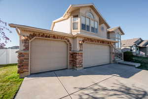 View of front of house with stone siding, driveway, a garage, and stucco siding
