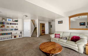 Carpeted living room with stairs and baseboards