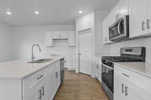 Kitchen with stainless steel appliances, recessed lighting, a center island with sink, light wood finished floors, and white cabinets