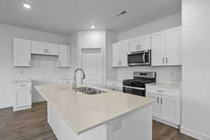 Kitchen featuring stainless steel appliances, an island with sink, white cabinetry, dark wood-style flooring, and recessed lighting