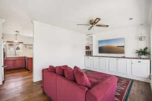 Living area featuring dark wood-style flooring, crown molding, a ceiling fan, built in shelves, and a textured ceiling