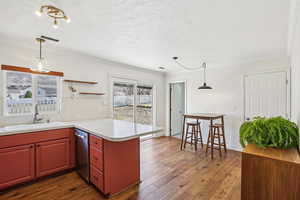Kitchen with light countertops, a peninsula, pendant lighting, dark wood-style flooring, and crown molding