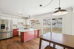 Dual tone kitchen with hanging light fixtures, stainless steel fridge with ice dispenser, light countertops, electric range, and ornamental molding
