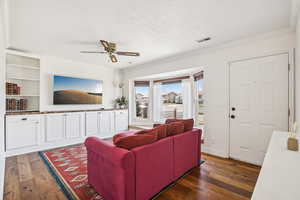 Living room with dark wood-style flooring, a ceiling fan, ornamental molding, and a textured ceiling