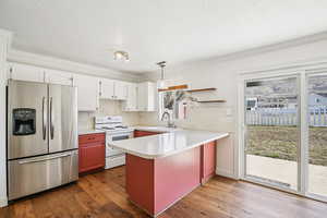 Two tone kitchen featuring stainless steel fridge with ice dispenser, electric stove, light countertops, hanging light fixtures, and a peninsula