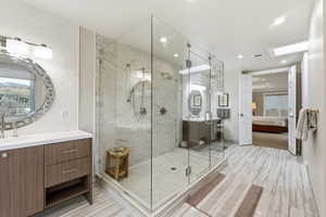 Ensuite bathroom with a marble finish shower, vanity, light wood finished floors, recessed lighting, and backsplash