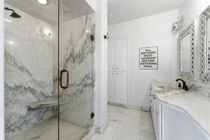 Full bathroom featuring vanity, a marble finish shower, and light marble finish flooring