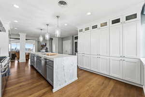Dual tone kitchen with stainless steel appliances, hanging light fixtures, glass fronted cabinets, dark wood-style floors, and dual tone cabinetry