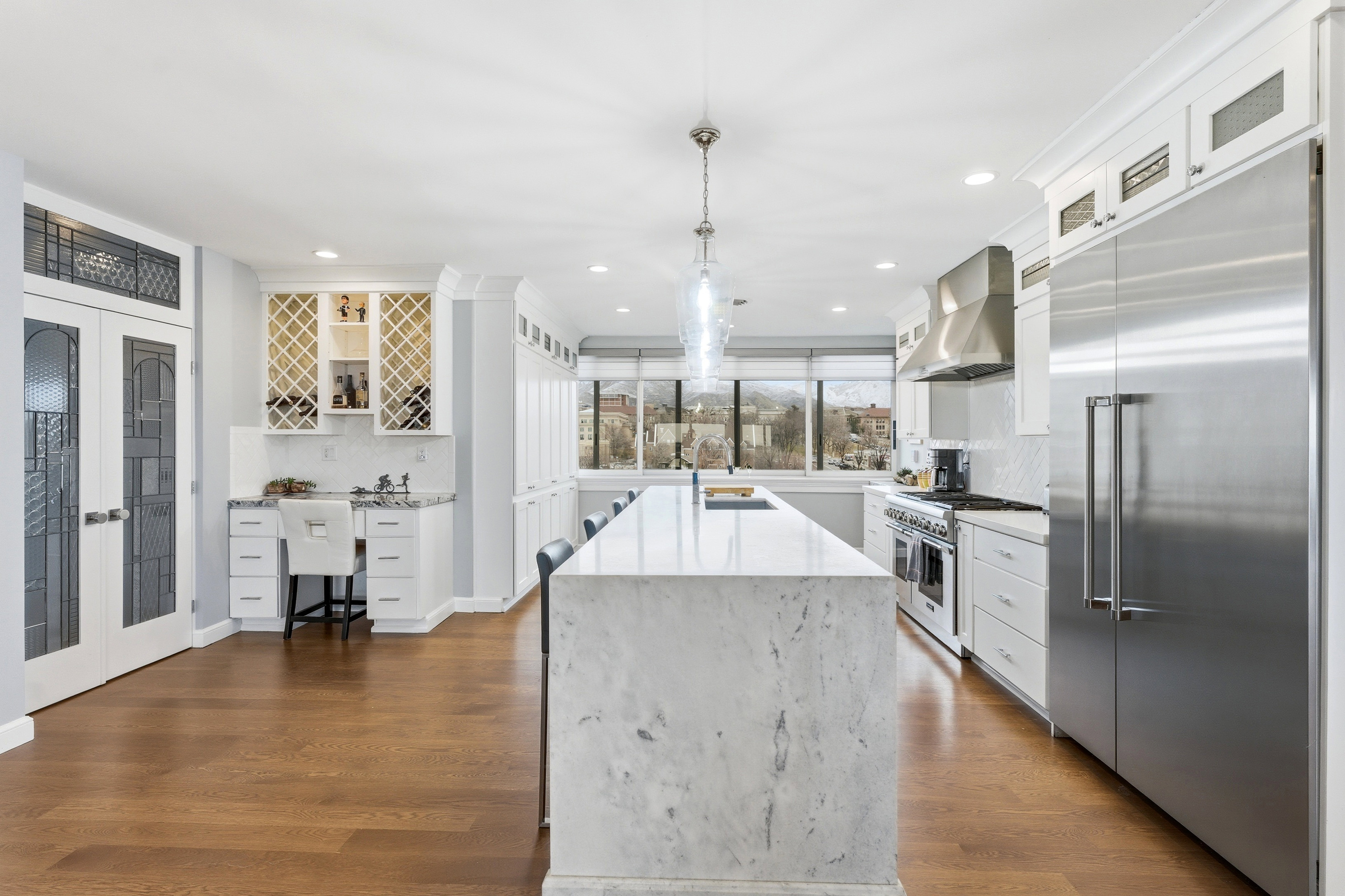 Kitchen with white cabinets, premium appliances, glass insert cabinets, light stone countertops, and dark wood-style flooring
