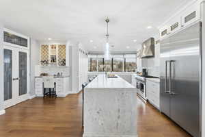 Kitchen with white cabinets, premium appliances, glass insert cabinets, light stone countertops, and dark wood-style flooring