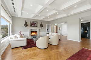 Living room featuring parquet flooring, a premium fireplace, coffered ceiling, crown molding, and recessed lighting