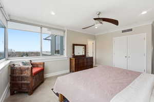 Bedroom with light colored carpet, crown molding, ceiling fan, and a closet