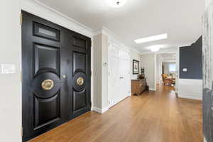 Foyer featuring light wood-type flooring, ornamental molding, and wainscoting