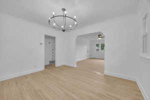 Unfurnished dining area featuring light wood finished floors, hanging lights, crown molding, a ceiling fan, and a textured ceiling
