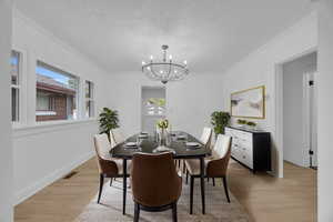 Dining space with light wood-style flooring, plenty of natural light, a chandelier, and ornamental molding
