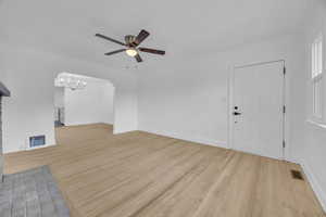 Unfurnished living room with ceiling fan, light wood-style floors, hanging lights, and a brick fireplace