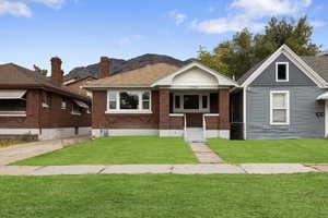 View of front facade featuring a front yard, covered porch, a mountain view, roof with shingles, and brick siding
