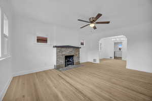 Unfurnished living room with light wood-style floors, a ceiling fan, a fireplace, ornamental molding, and a chandelier