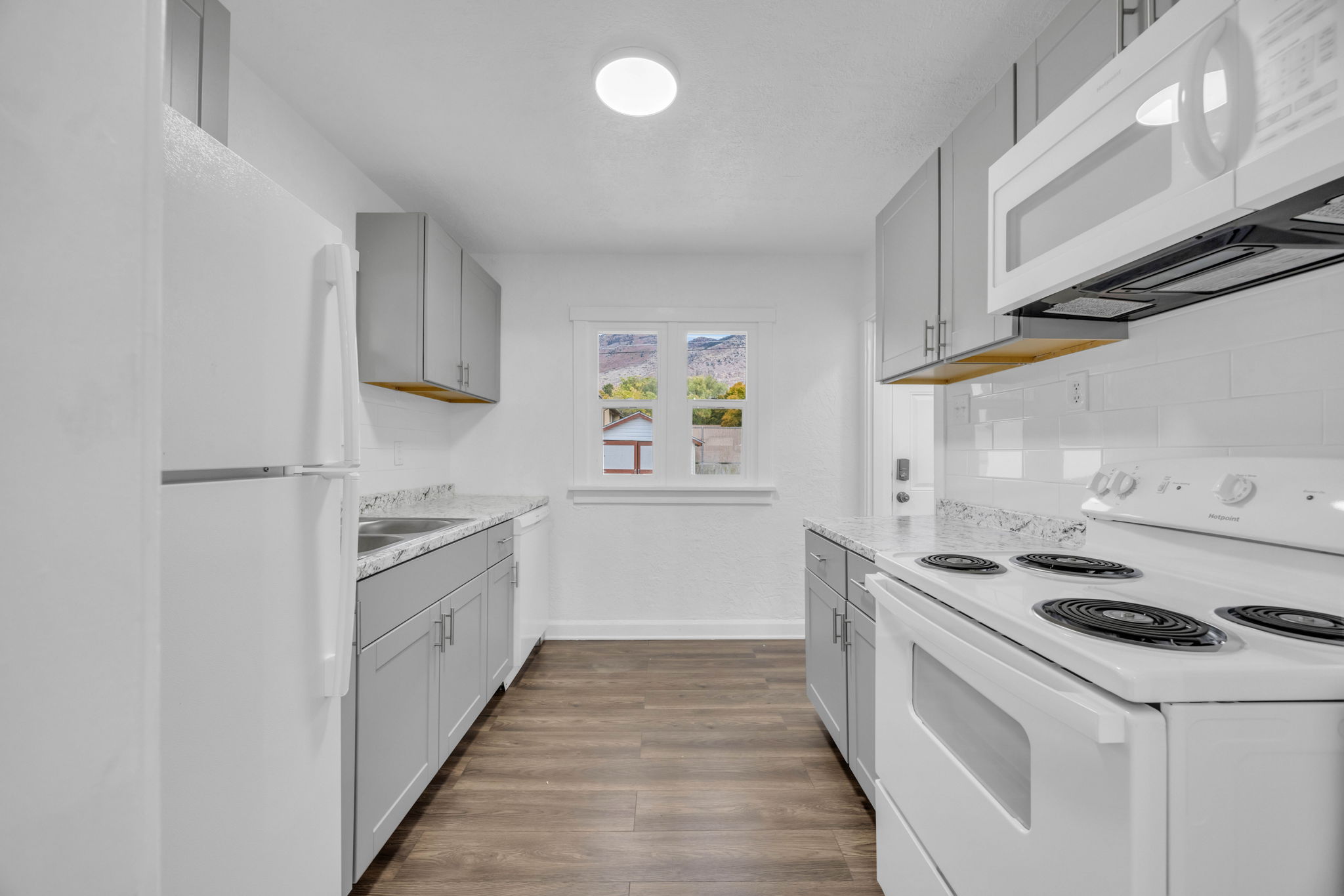 Kitchen featuring white appliances, gray cabinetry, light countertops, dark wood finished floors, and decorative backsplash